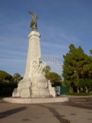 A big statue by a nice park, with a ferris wheel in the background