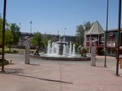 A Fountain, Two Statues And The Bridge In The Background